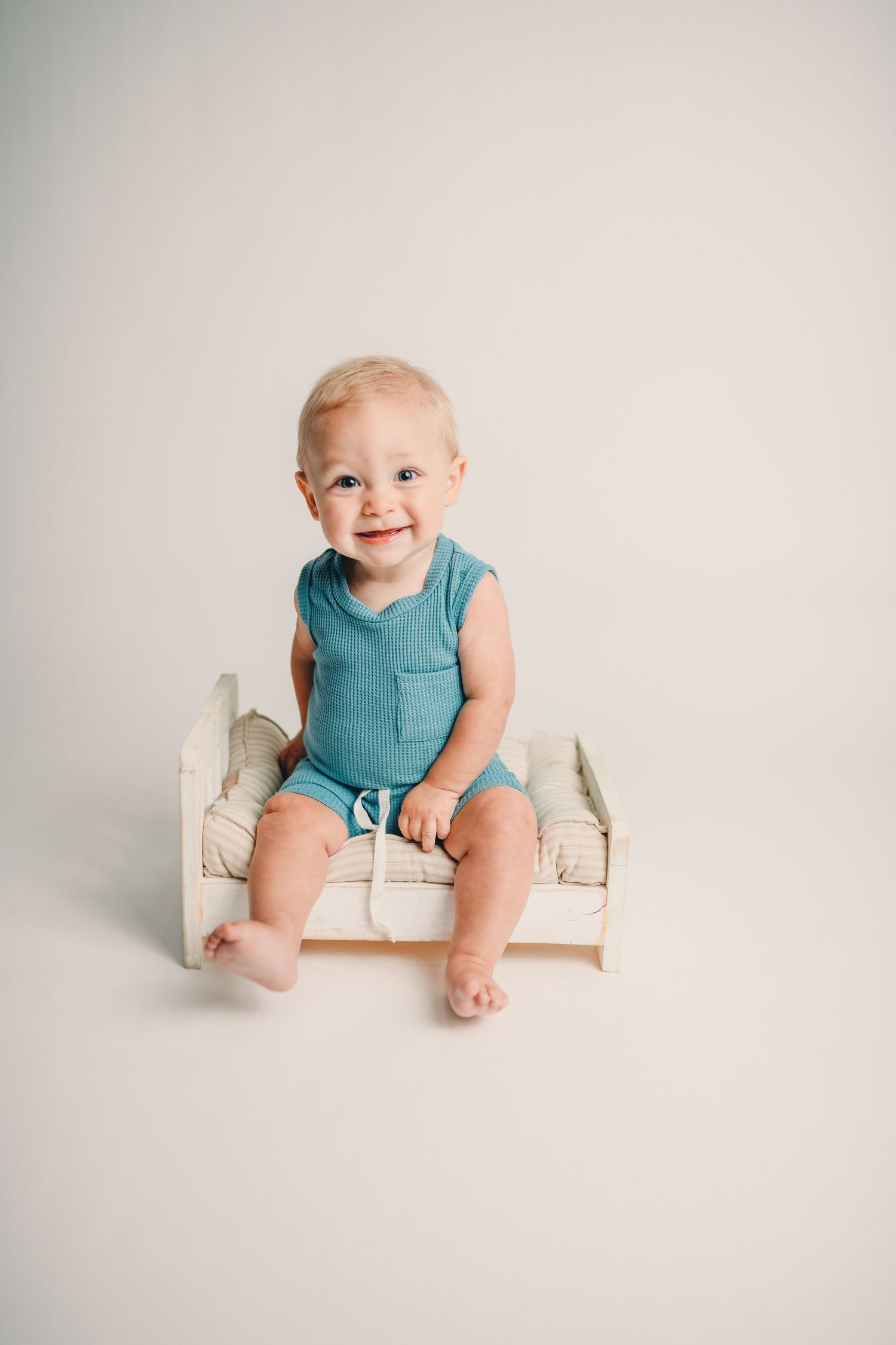 Minimalist baby photo session with white bench against light neutral background.