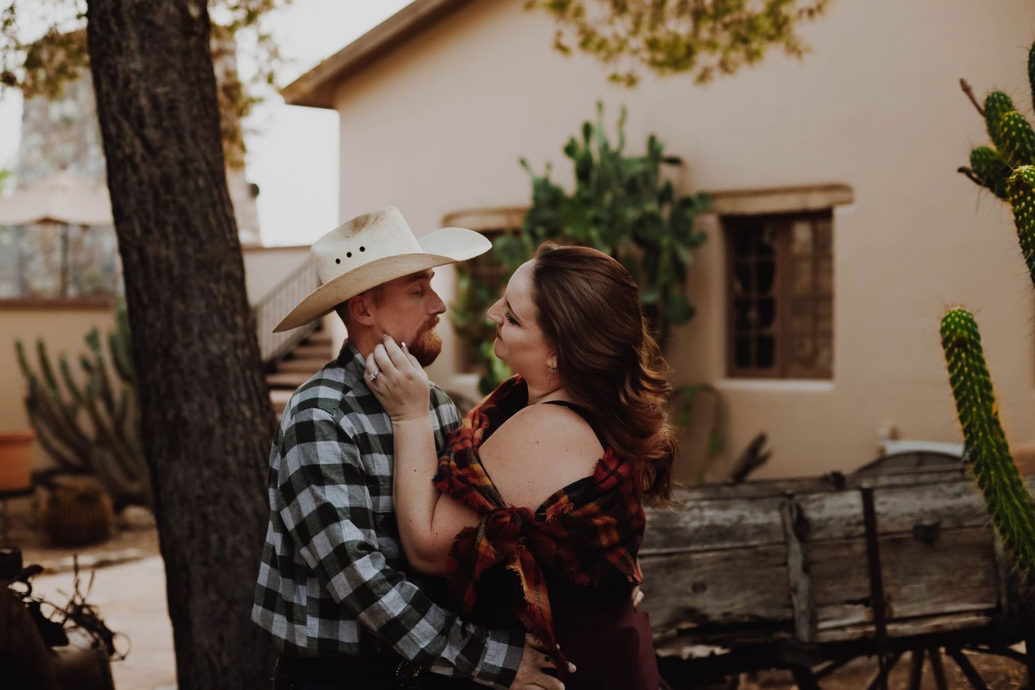 A couple in western and plaid attire share a tender moment outdoors.