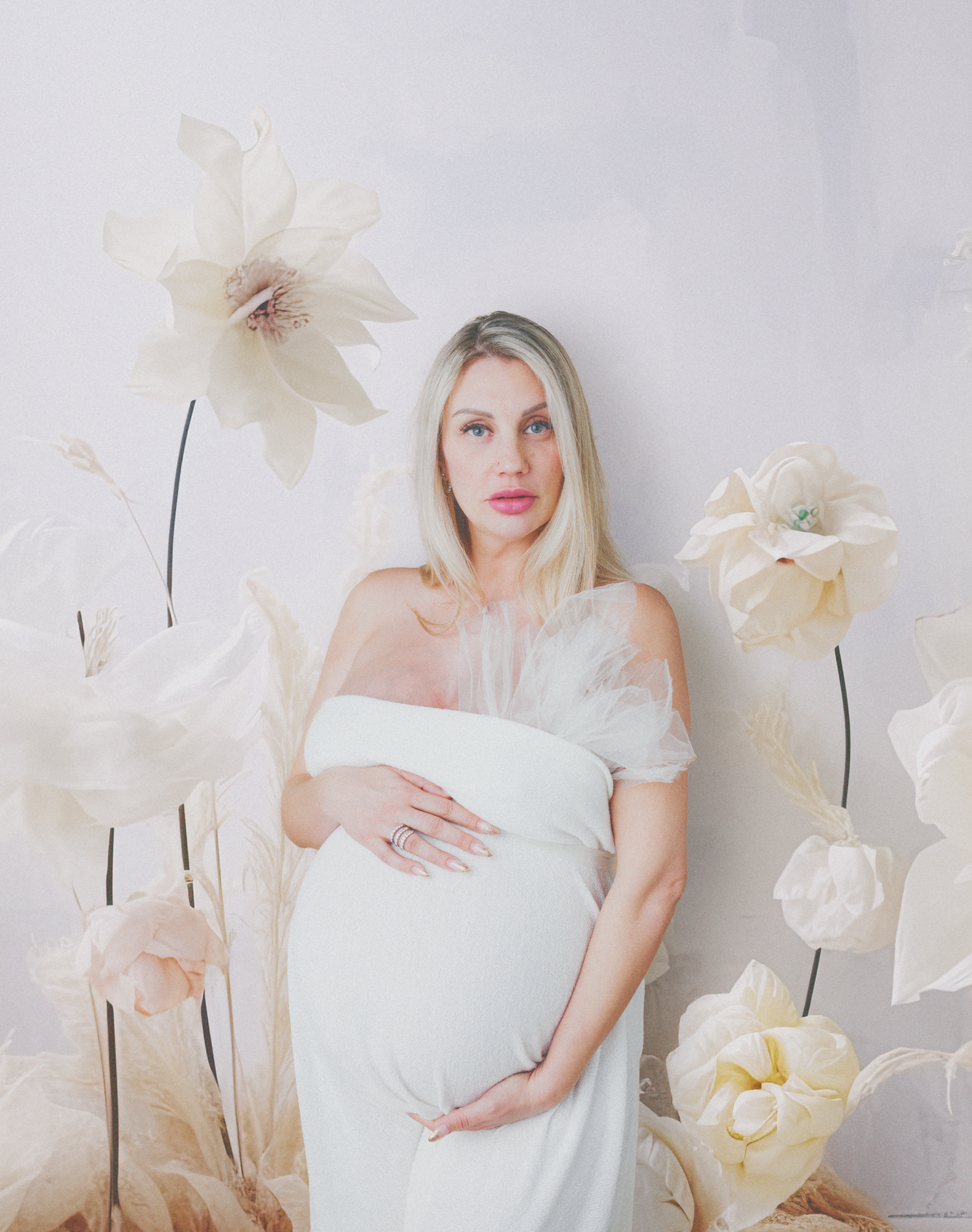 Elegant maternity portrait with dreamy white paper flowers surrounding a figure in a graceful off-shoulder gown.