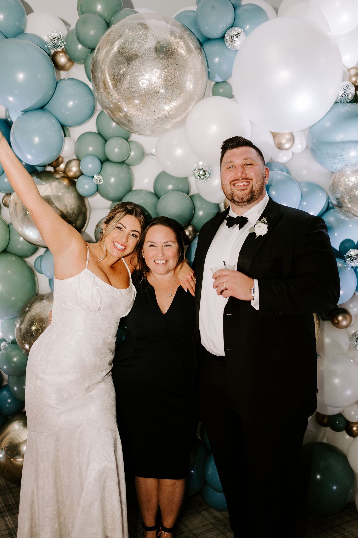 Wedding party poses under an elegant arch of blue, white, and silver balloons.