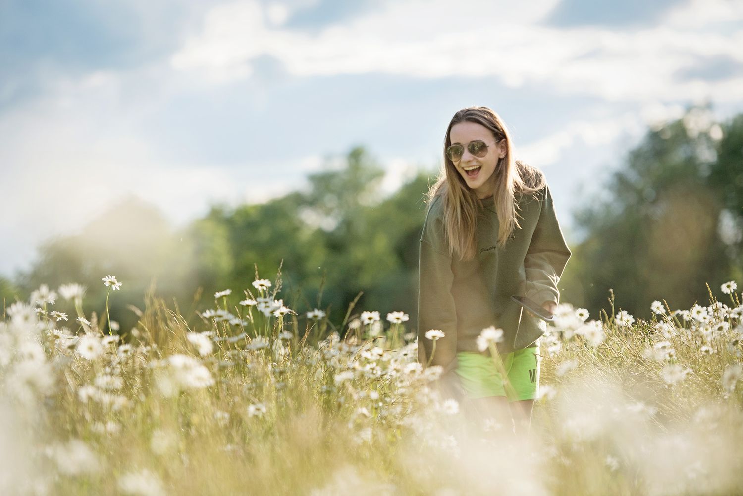 Woman in casual attire standing among blooming white wildflowers during golden hour.