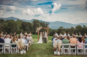 Panoramic view of an outdoor wedding ceremony with mountain landscape and white chairs.