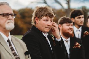 Wedding guests and groomsmen in formal attire gather during an autumn outdoor ceremony.