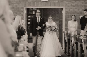 Indoor wedding ceremony procession in a brick-walled venue with traditional decor.