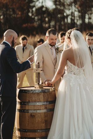 Wedding ceremony featuring rustic wooden barrels and a bride in a flowing white lace gown.