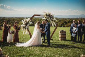 Panoramic view of an outdoor wedding ceremony setup in a scenic field with mountains in the background.