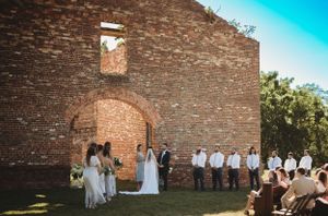Wedding ceremony setup against a rustic brick wall under blue sky.