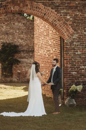 Wedding couple shares intimate moment against rustic brick wall backdrop.