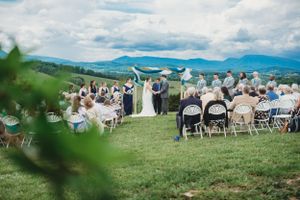 A scenic outdoor wedding ceremony on a hilltop with mountain views and white chairs set up for guests.