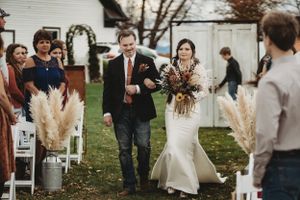 Wedding guests and wedding party gather for an outdoor ceremony with rustic decor and pampas grass.