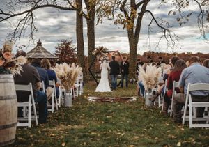 Wide shot of outdoor wedding ceremony setup with white chairs and fall trees in the background.