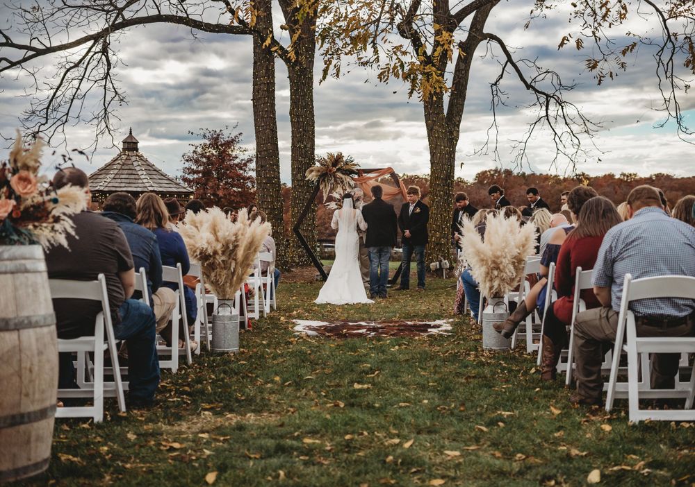 Wide shot of outdoor wedding ceremony setup with white chairs and fall trees in the background.