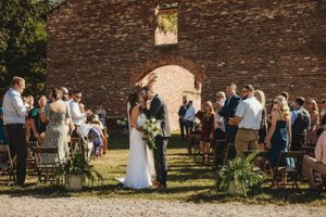 Outdoor wedding ceremony with guests seated by ancient brick wall.
