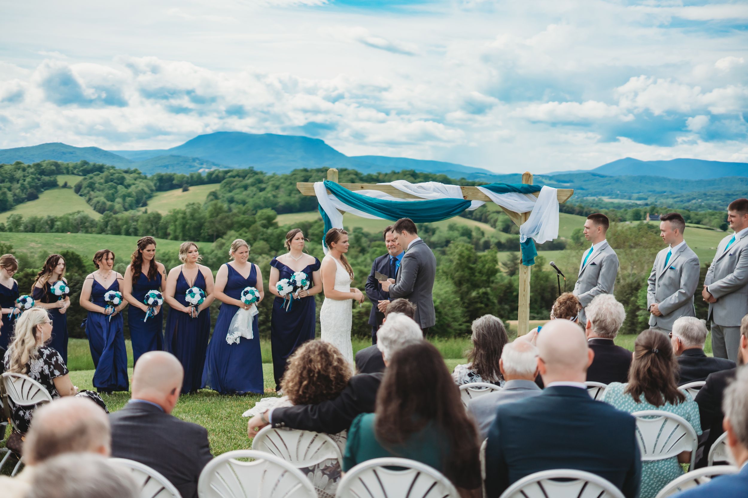 Panoramic view of wedding guests seated facing mountains under blue skies.