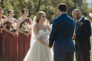 Wedding ceremony participants arranged in front of decorative floral arrangements and wooden barrels.
