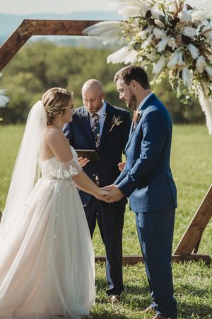 Intimate outdoor wedding ceremony with floral arch and wooden barrels as decor elements.