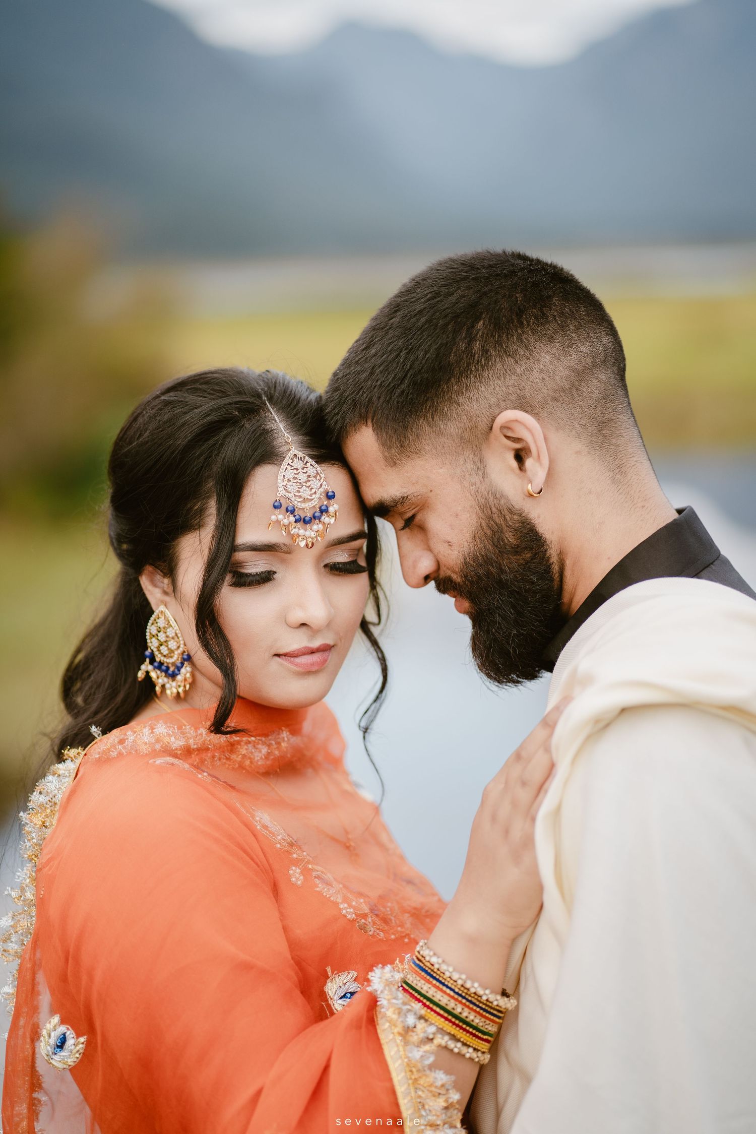 A romantic couple in traditional South Asian attire embracing against a mountain backdrop.