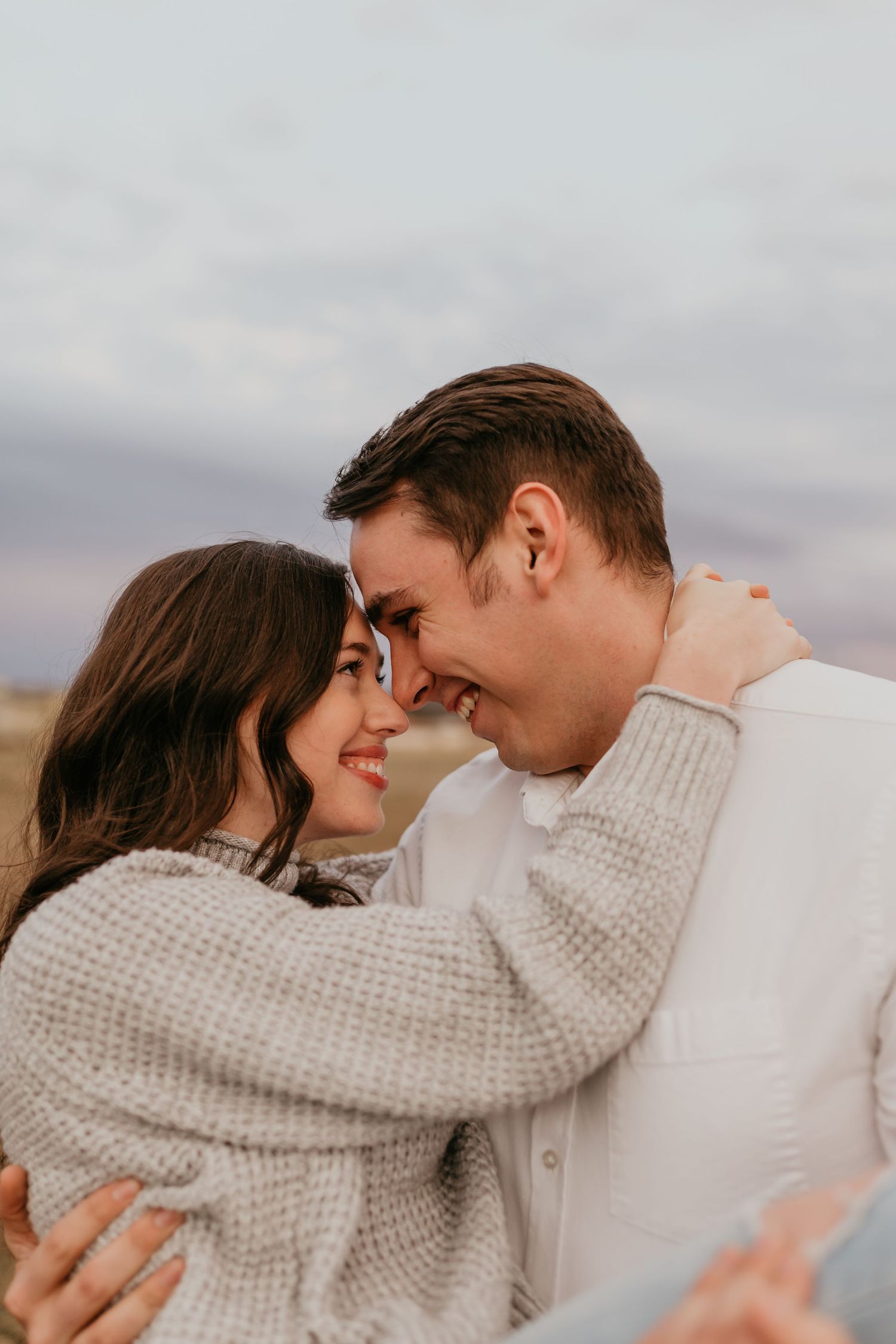 Close-up of smiling couple touching foreheads romantically outdoors in soft natural light.