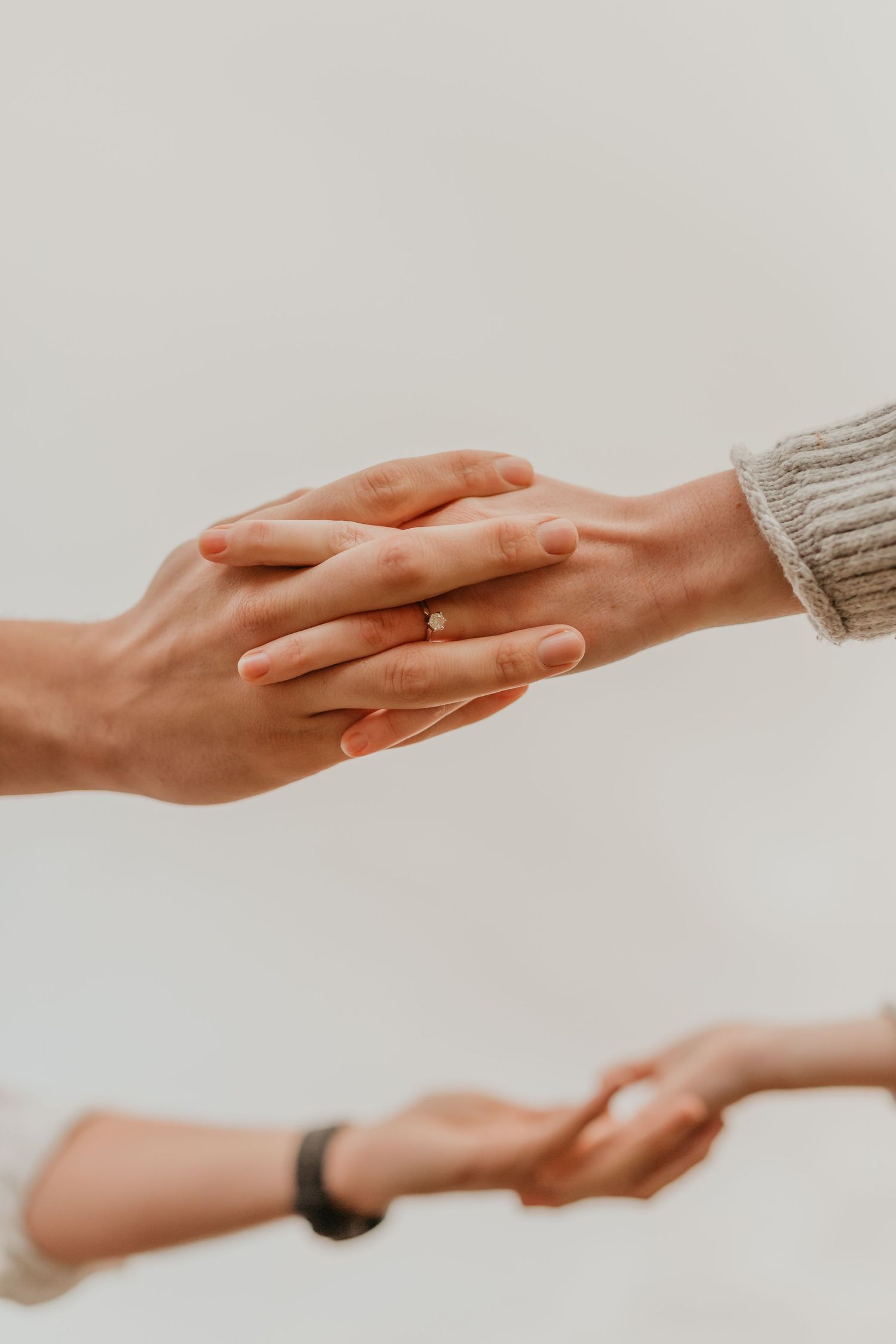 Two people holding hands tenderly, one wearing an engagement ring and a cozy knit sweater.