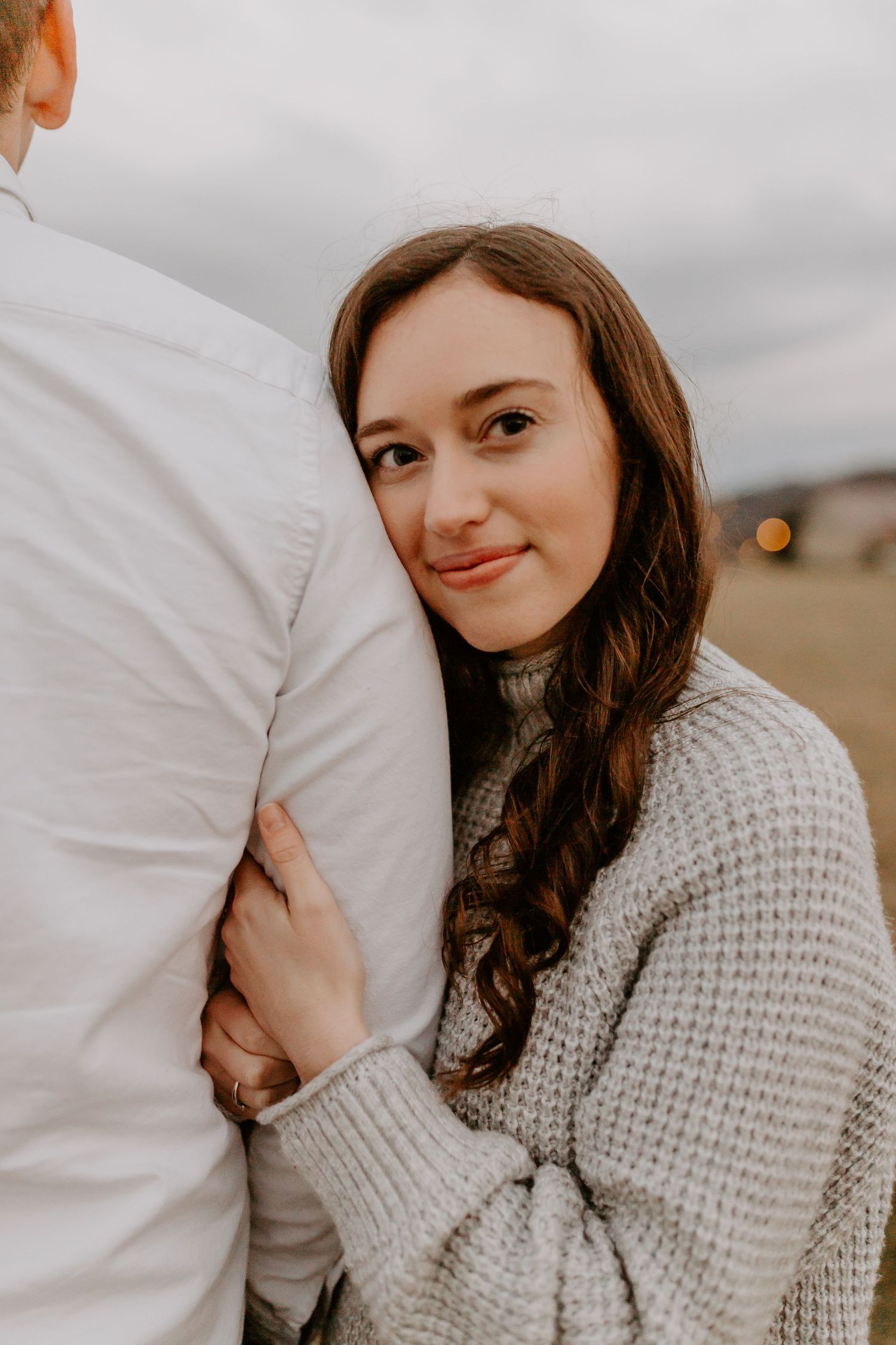 Woman hugging mans torso and looking at camera with a soft smile in an outdoor setting.
