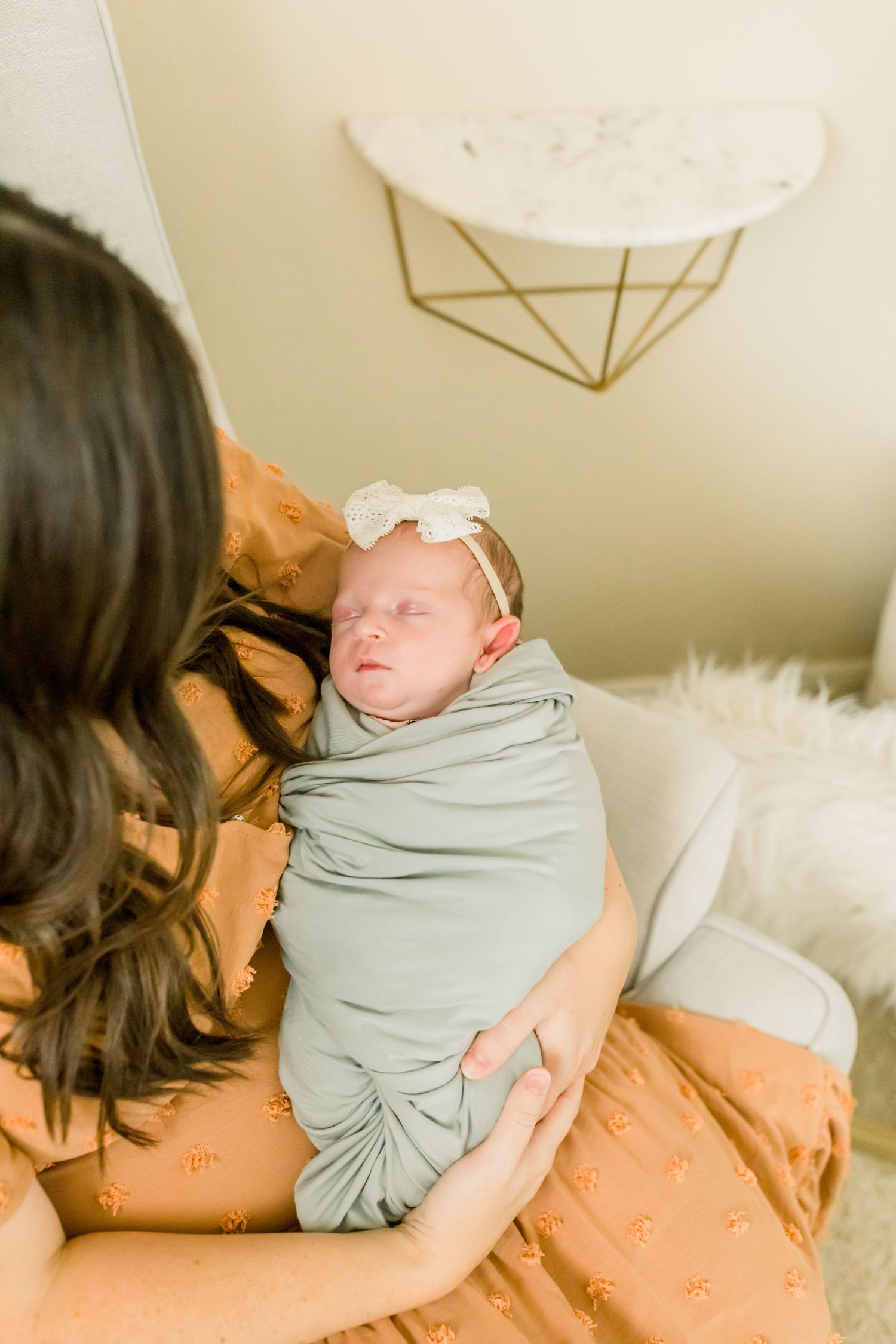 Sweet newborn moment captured in soft lighting with geometric wall decor.