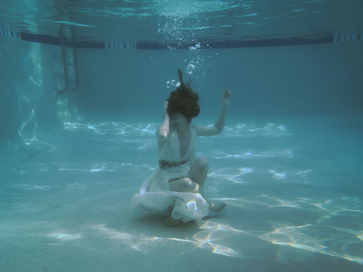 A woman in a white dress seated at the bottom of a pool