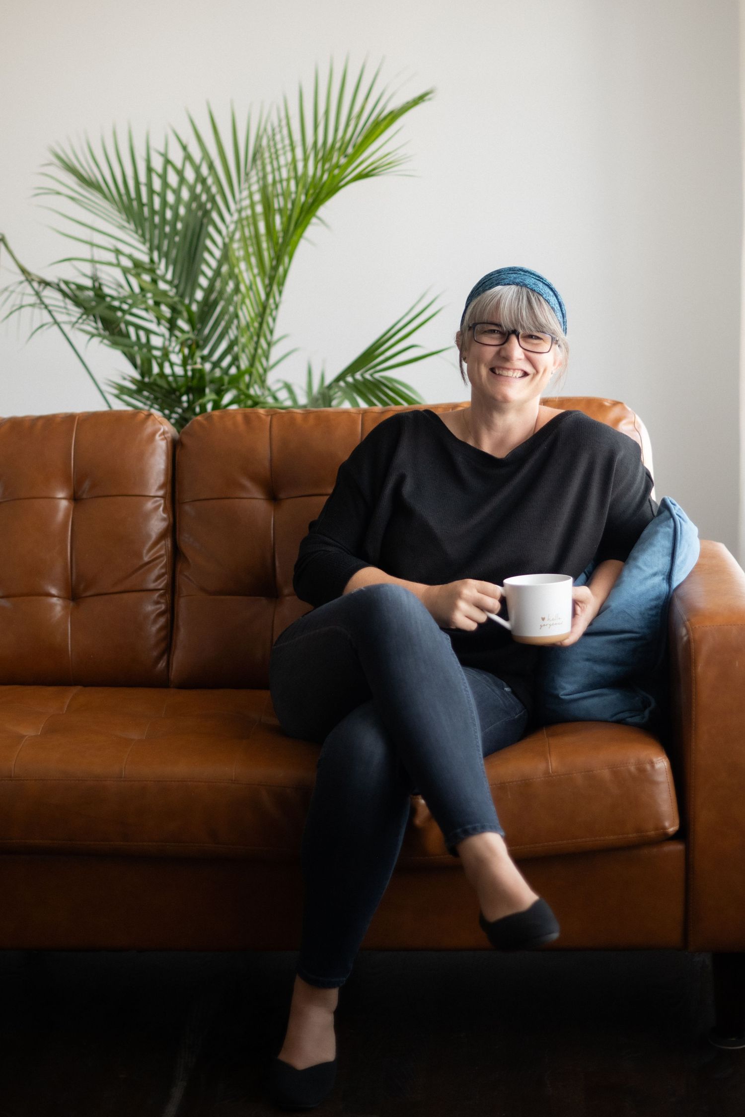Relaxed casual portrait on brown leather couch with tropical plant and coffee mug.