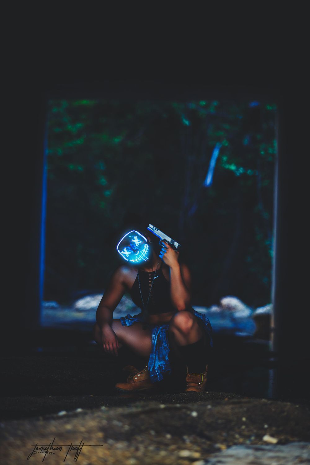 Sara squatting in light mask while holding handgun to her head