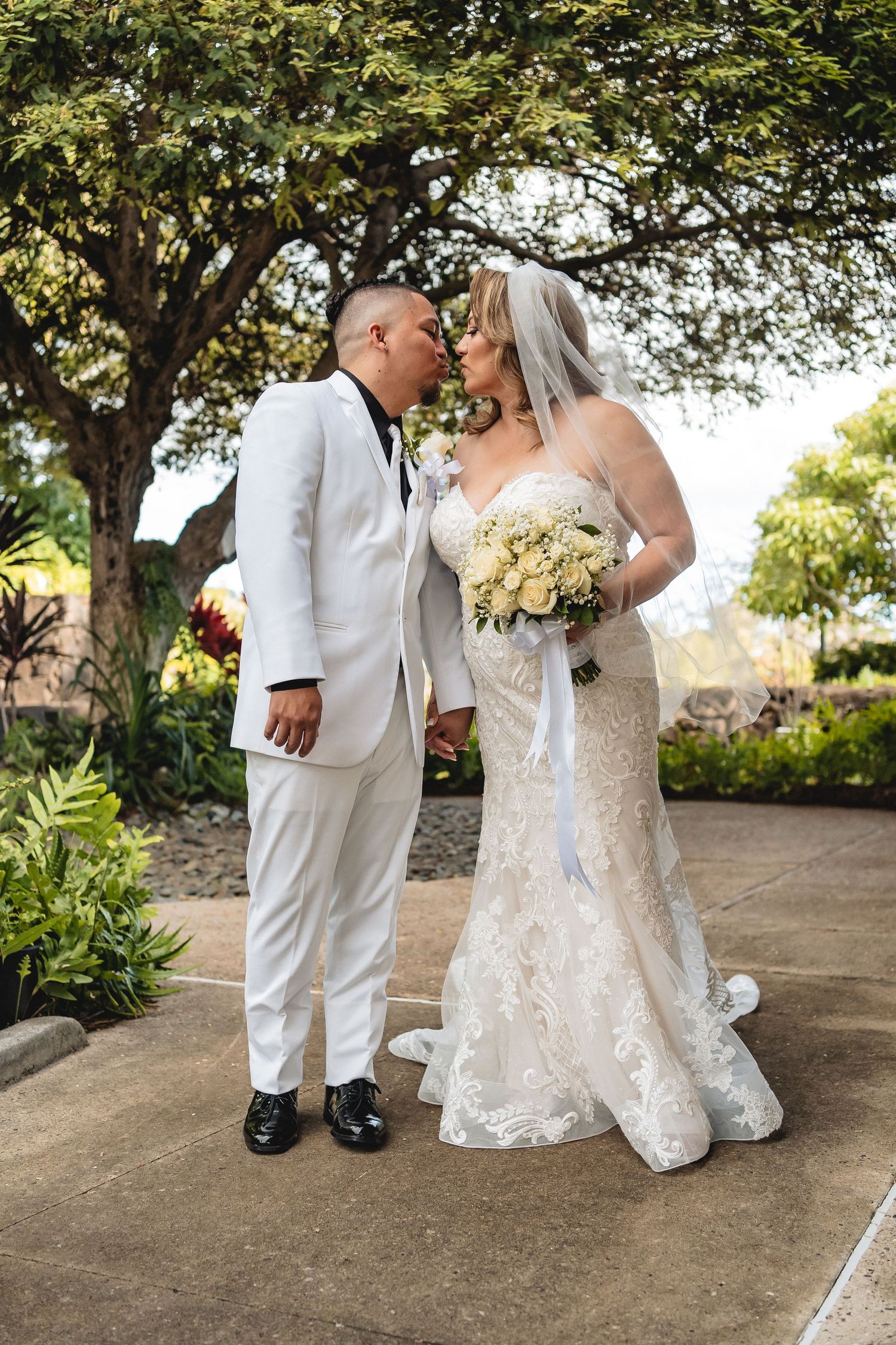 Couple in matching white attire share an intimate moment during their outdoor wedding photoshoot.