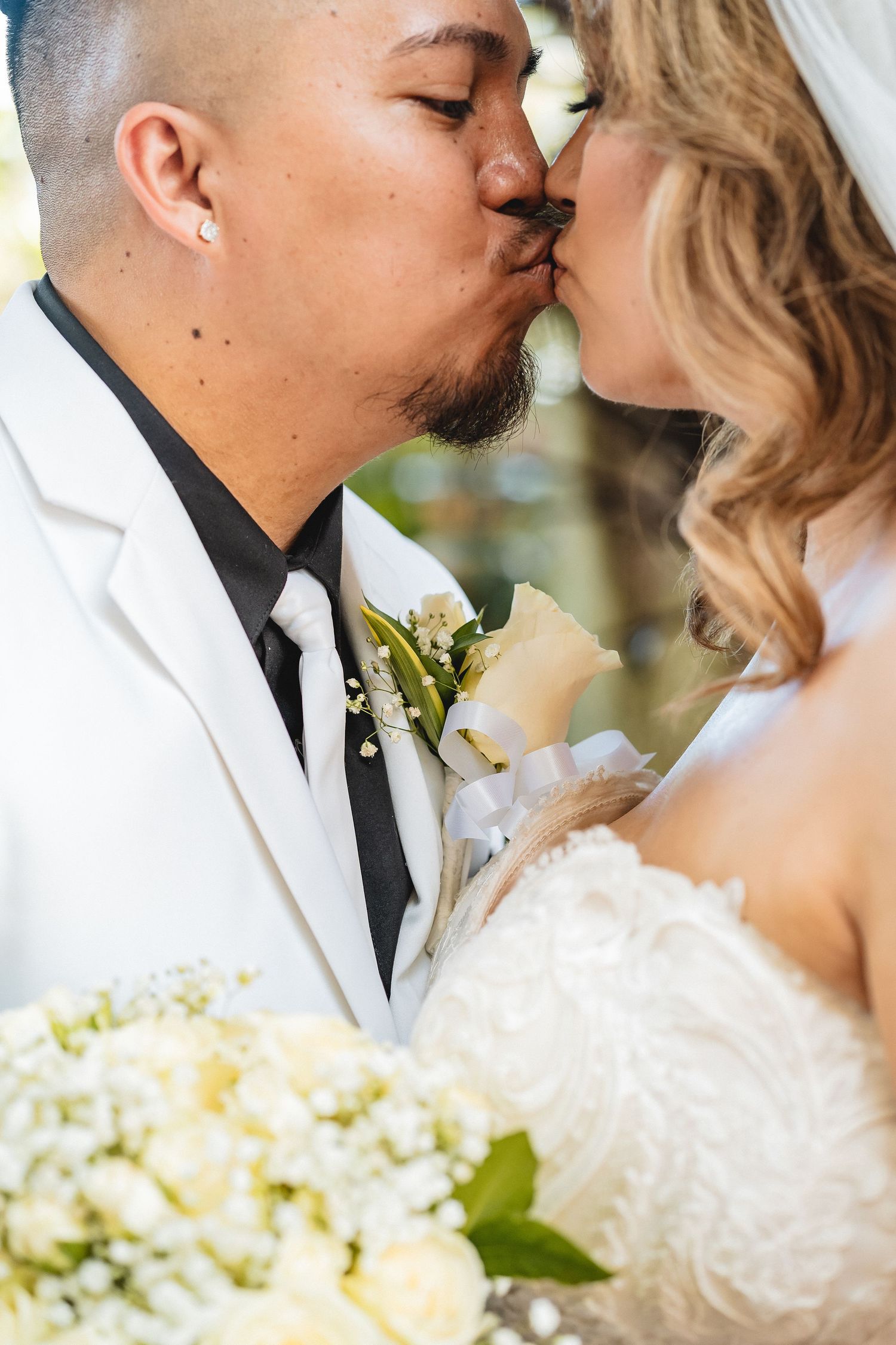 Close-up of newlyweds sharing an intimate kiss with white floral bouquet in view.