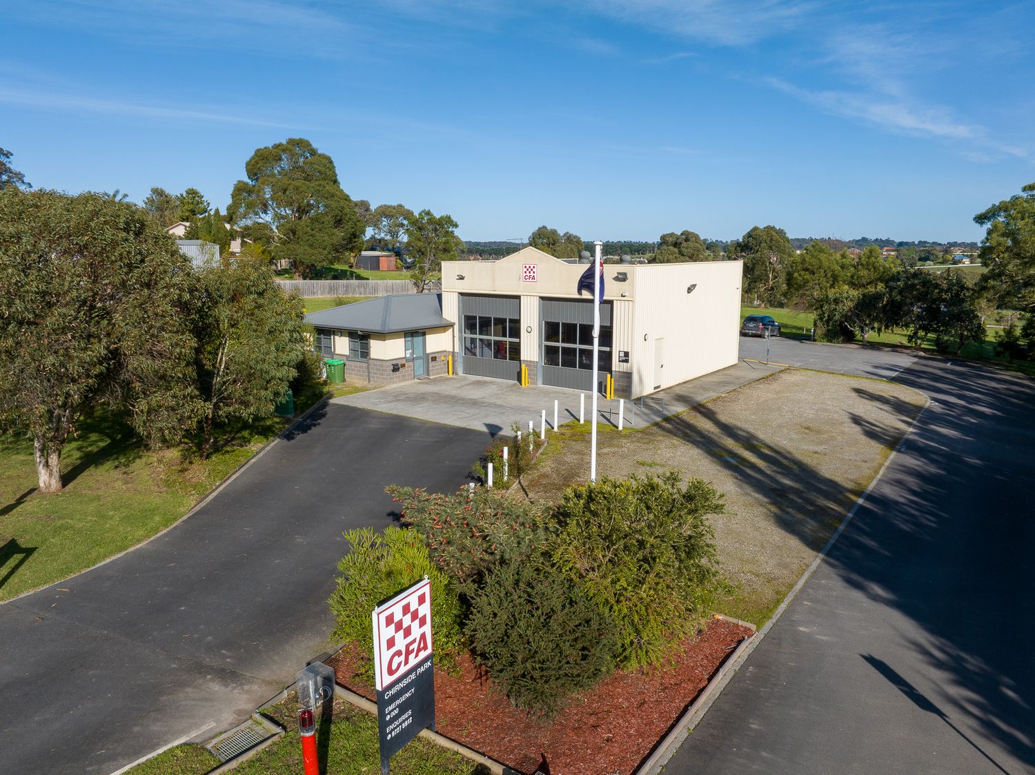 Aerial view of commercial industrial building with car park surrounded by trees.
