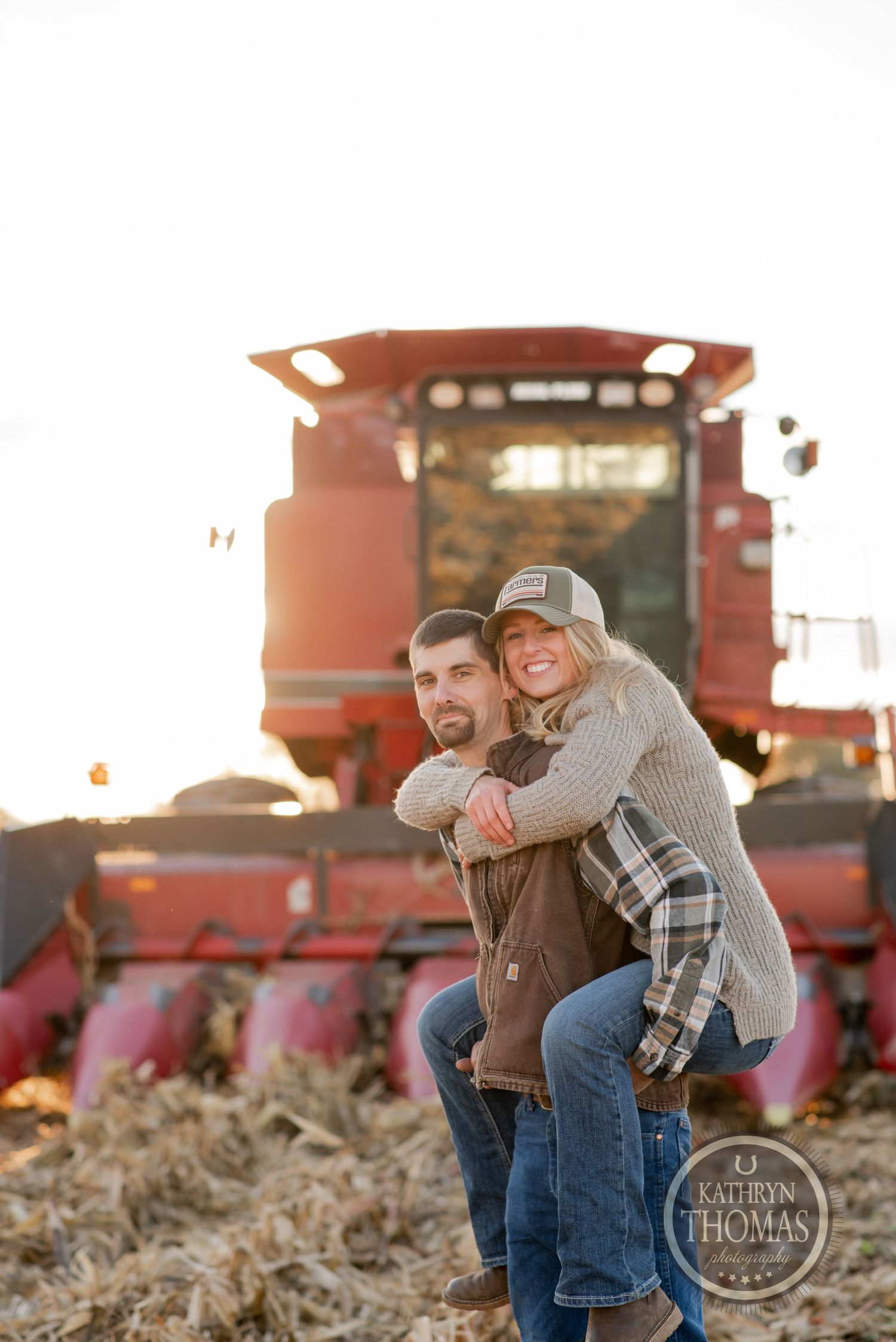 Couple sharing a piggyback ride in front of red combine harvester.
