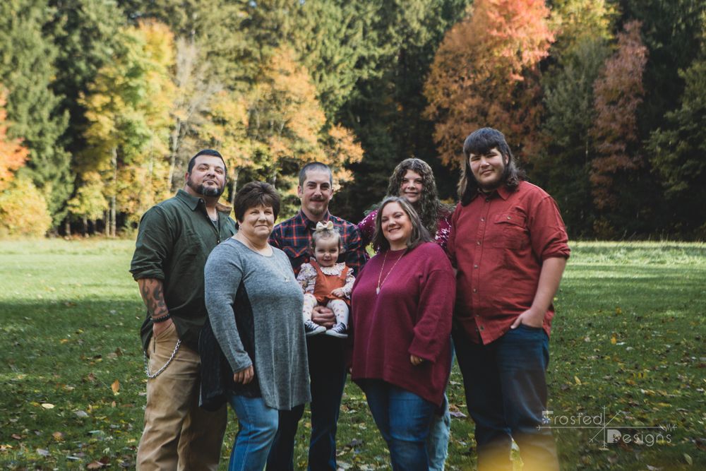 Extended family in open field in front of fall wooded colors.