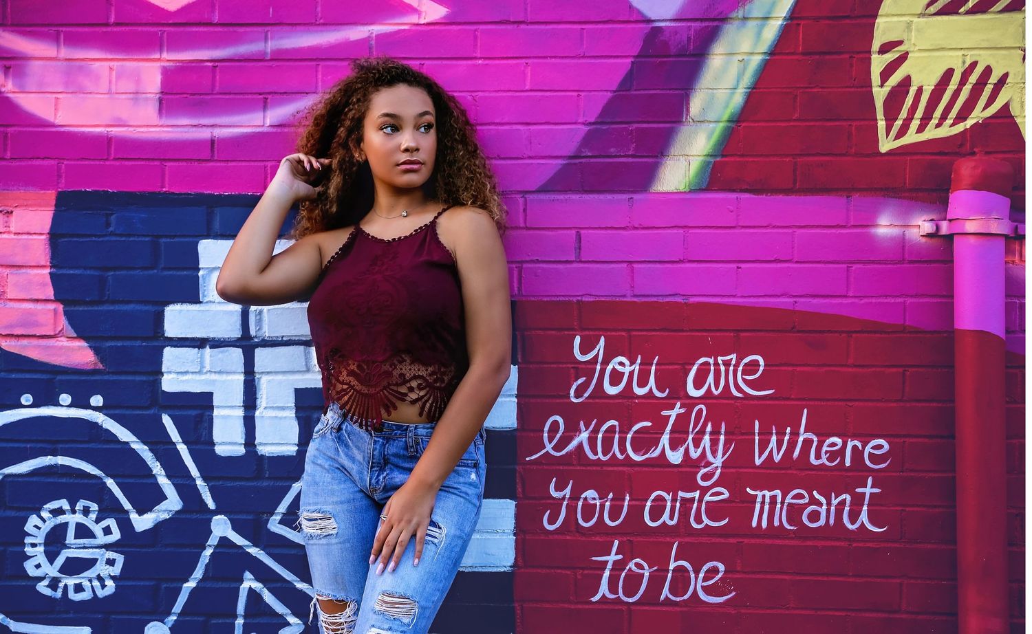 Stylish urban photoshoot against vibrant pink graffiti wall with inspirational text.