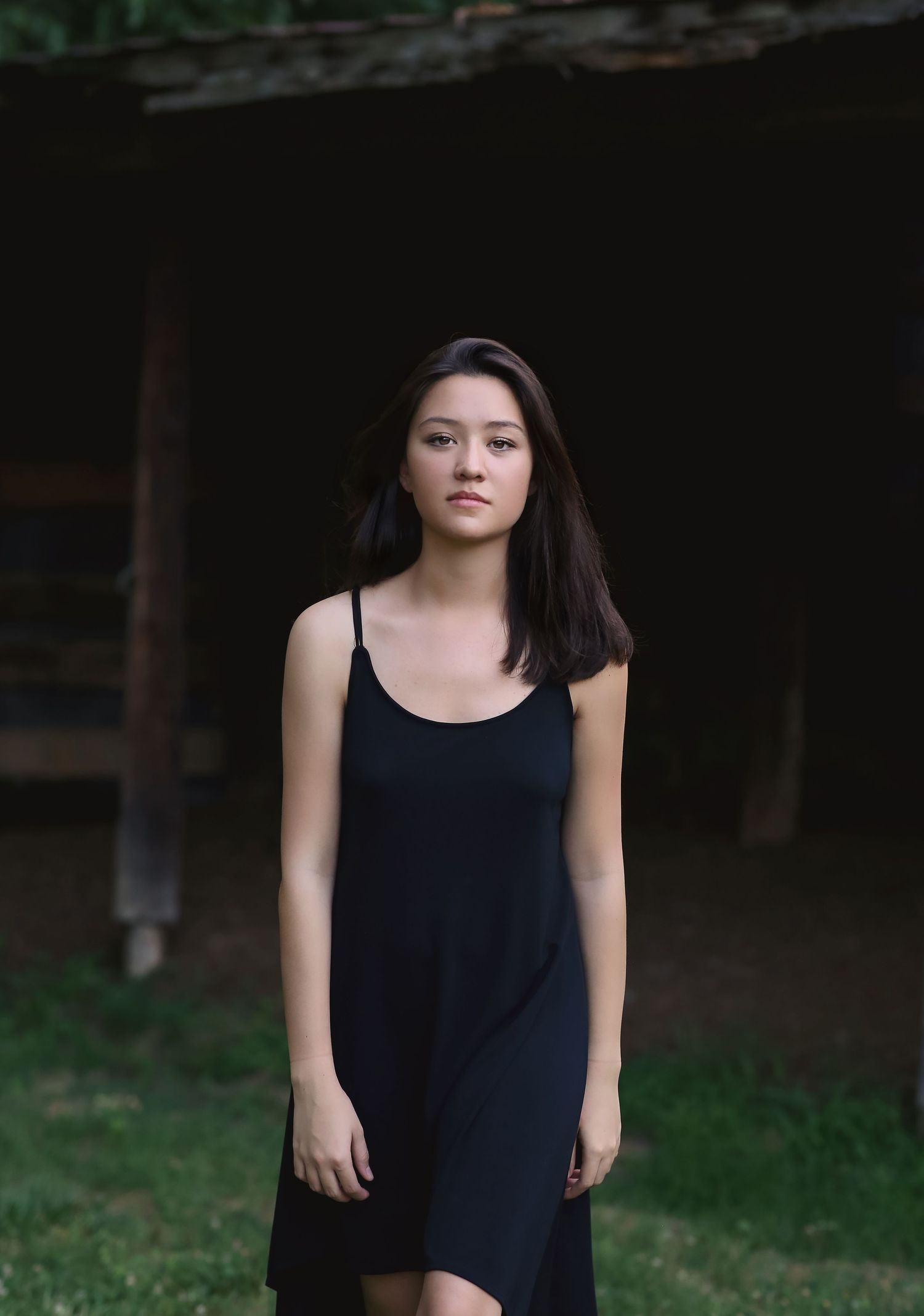 A portrait of a woman in a black dress standing against a dark background.