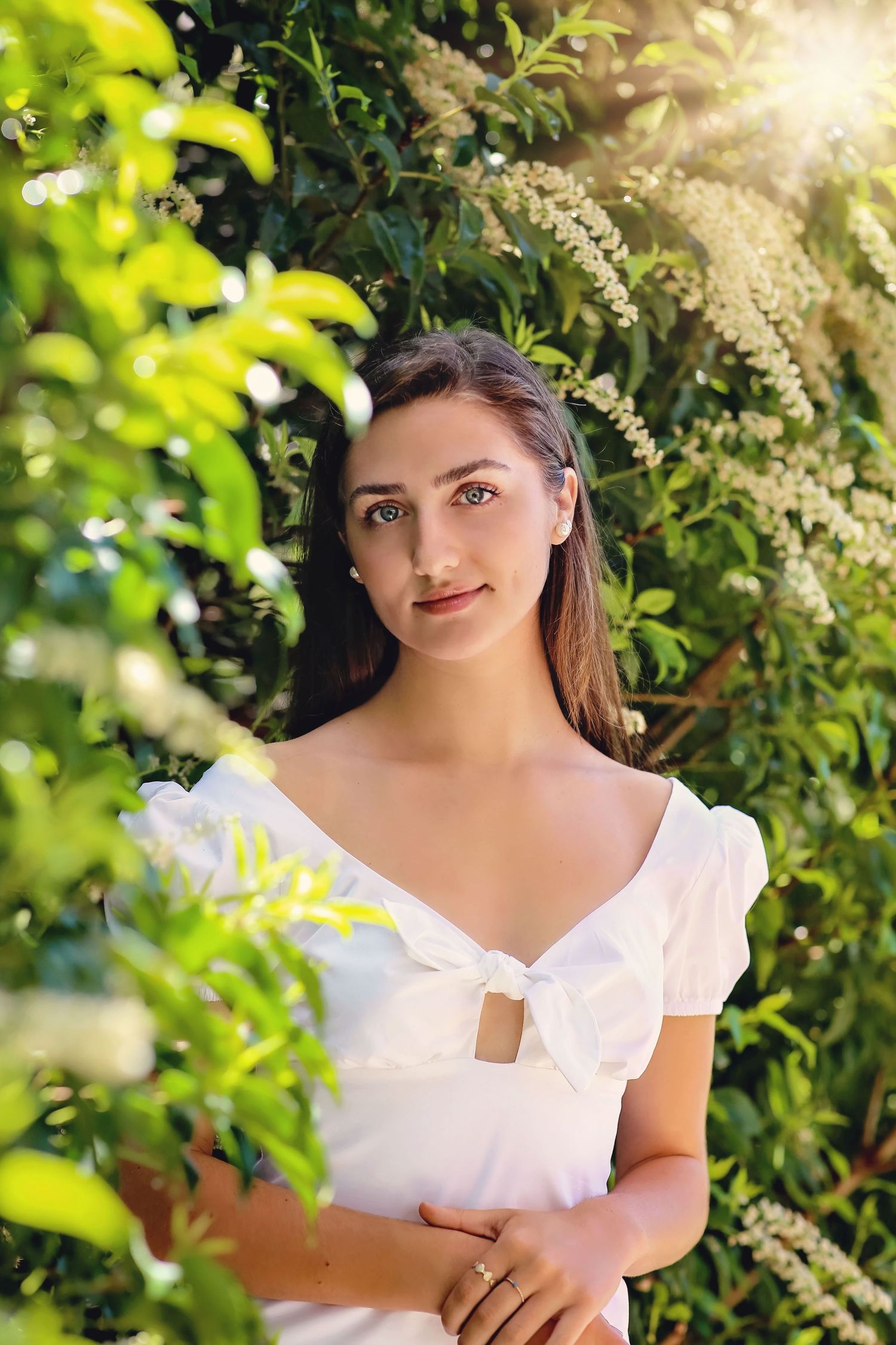 Summer portrait in a garden with sunlit greenery and white dress.