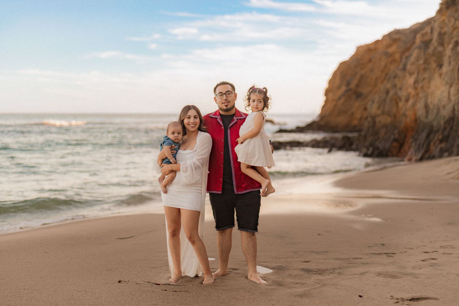 A family enjoys a sunny day together on a scenic beach with cliffs in the background.