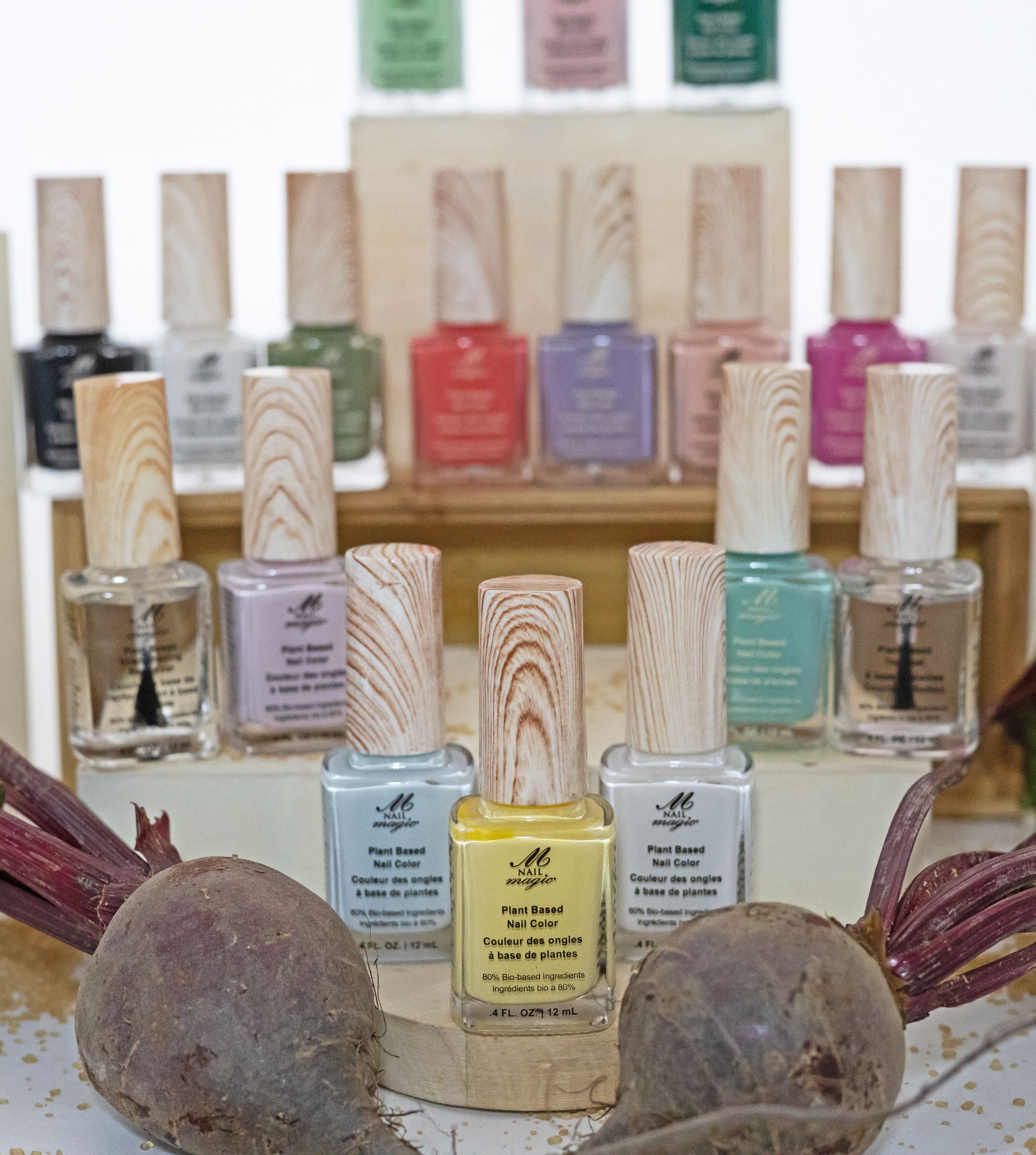 Collection of pastel nail polishes with wooden-textured caps arranged with purple beets.