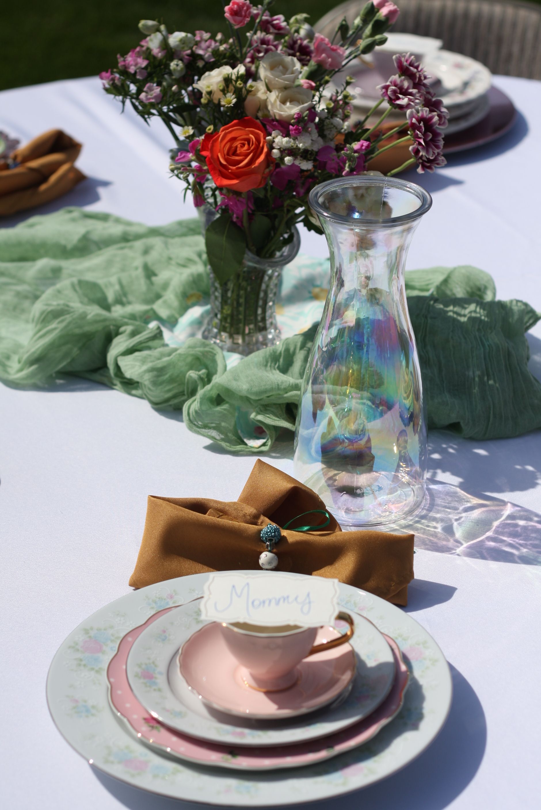 Elegant table setting with pink teacup, floral arrangement, and iridescent vase on white tablecloth.