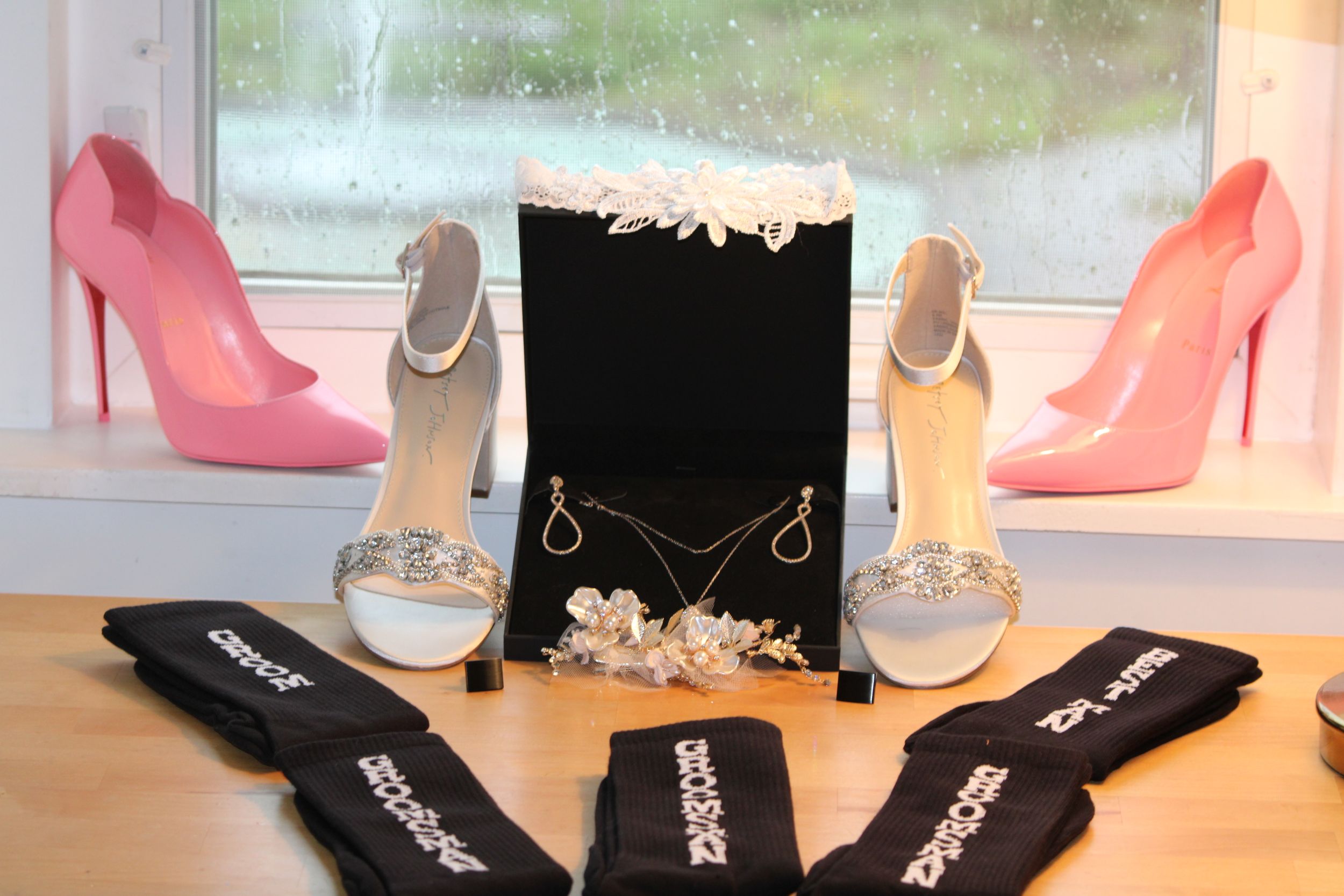 Wedding accessories display with pink and white heels, jewelry, and black velvet box on windowsill.