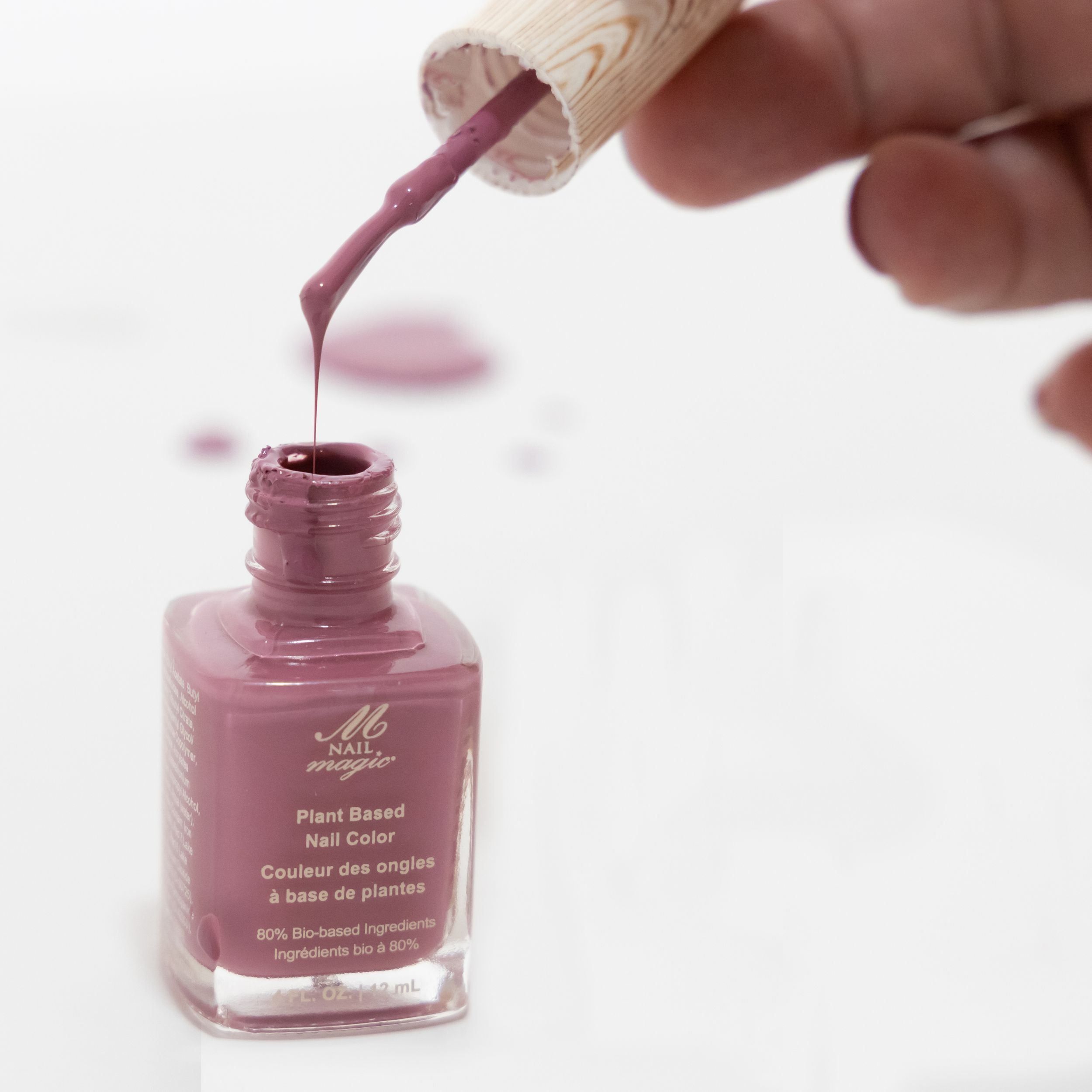 Mauve nail polish being dripped from brush into glass bottle against white background.