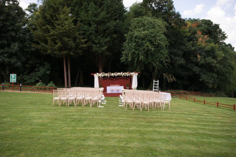 Outdoor wedding ceremony setup with white chairs and floral arch on a green lawn.