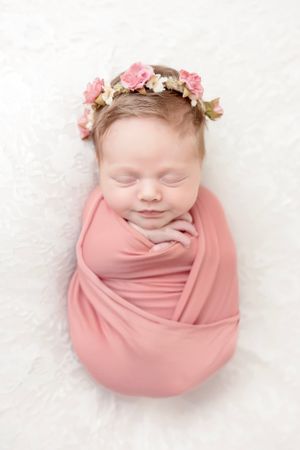 Sleeping newborn wrapped in soft pink fabric wearing delicate floral crown.