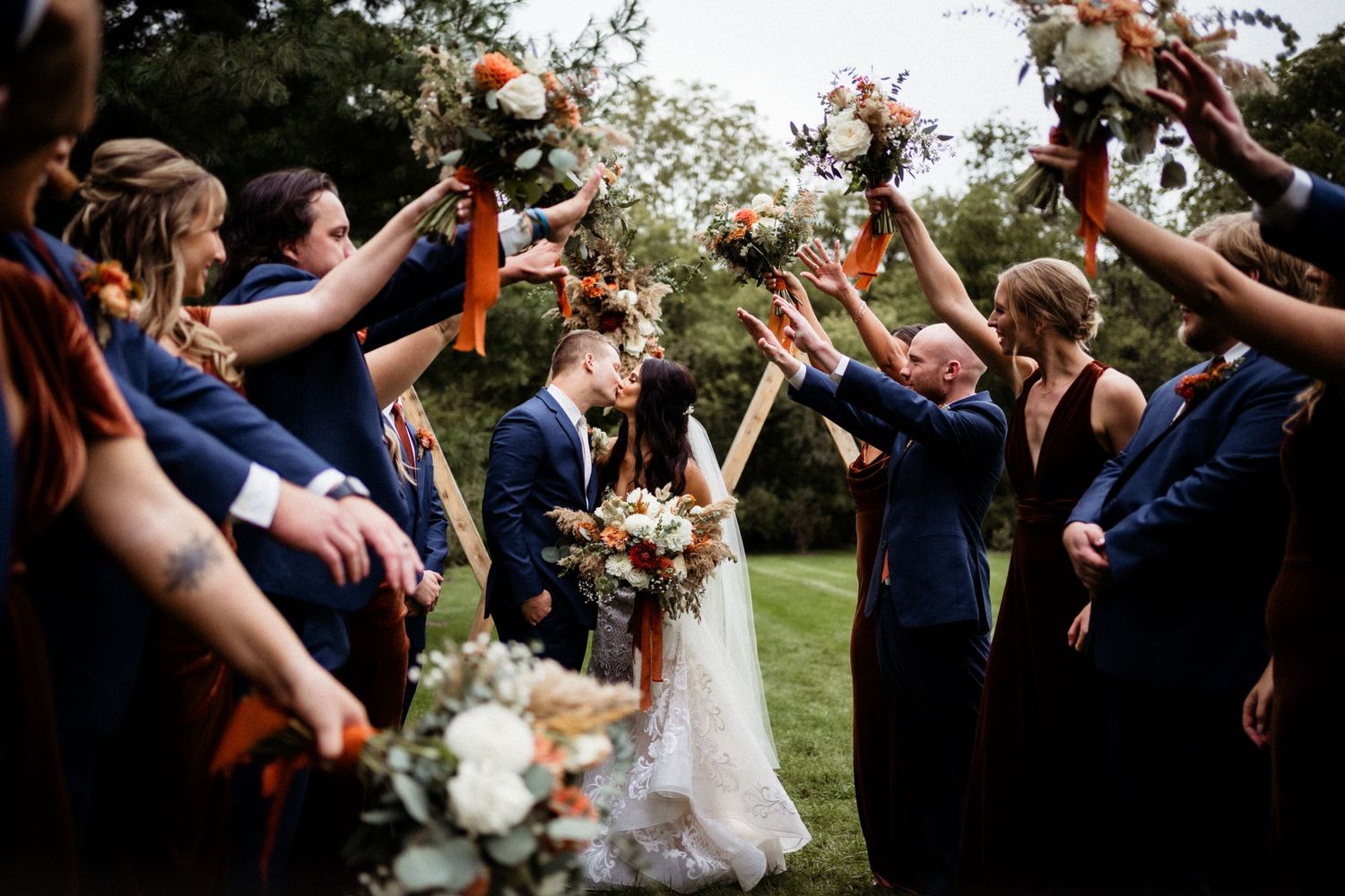 Wedding party celebrates with raised bouquets forming an arch over the newlyweds.