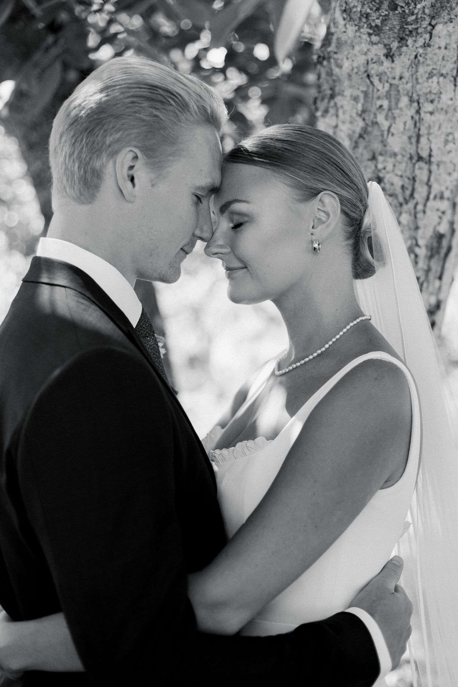 Romantic black and white portrait shot against tree backdrop.
