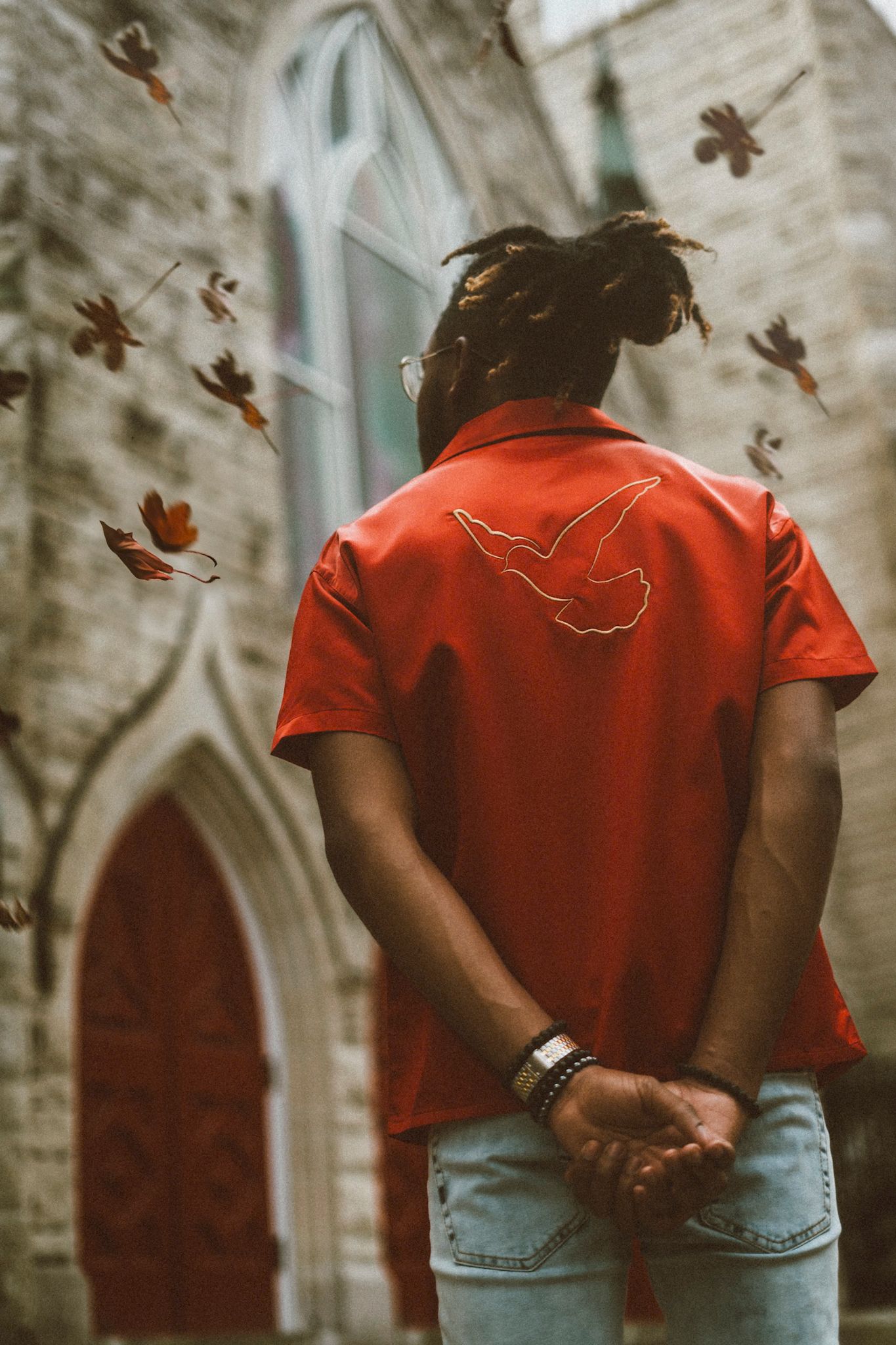 Red shirt with dove design photographed from behind at historic church with falling autumn leaves.