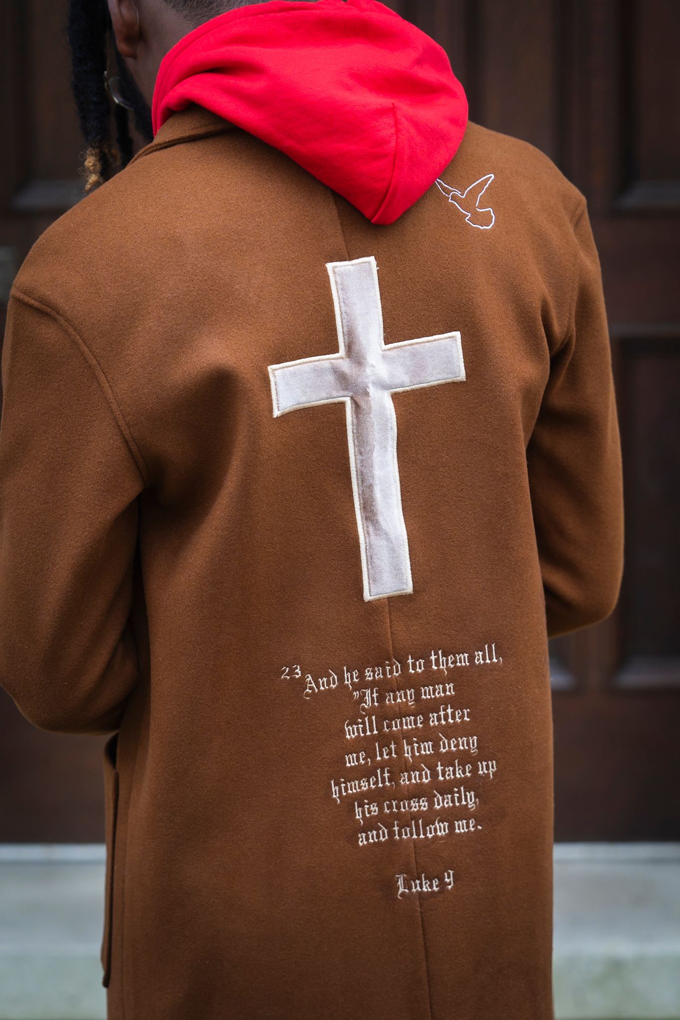 Brown jacket with white cross design and biblical verse on back.