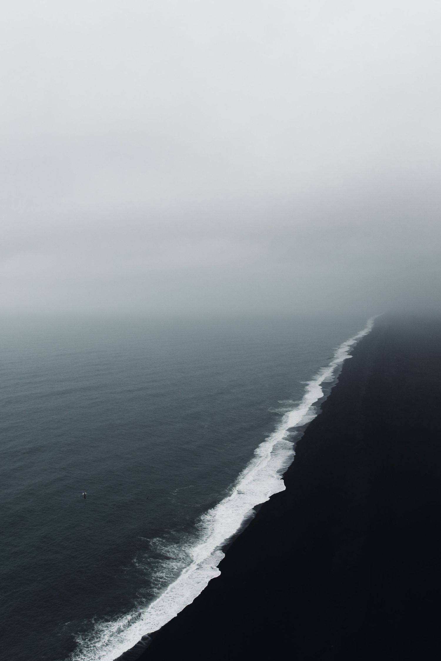 Aerial view of ocean waves creating white foam line against dark water.