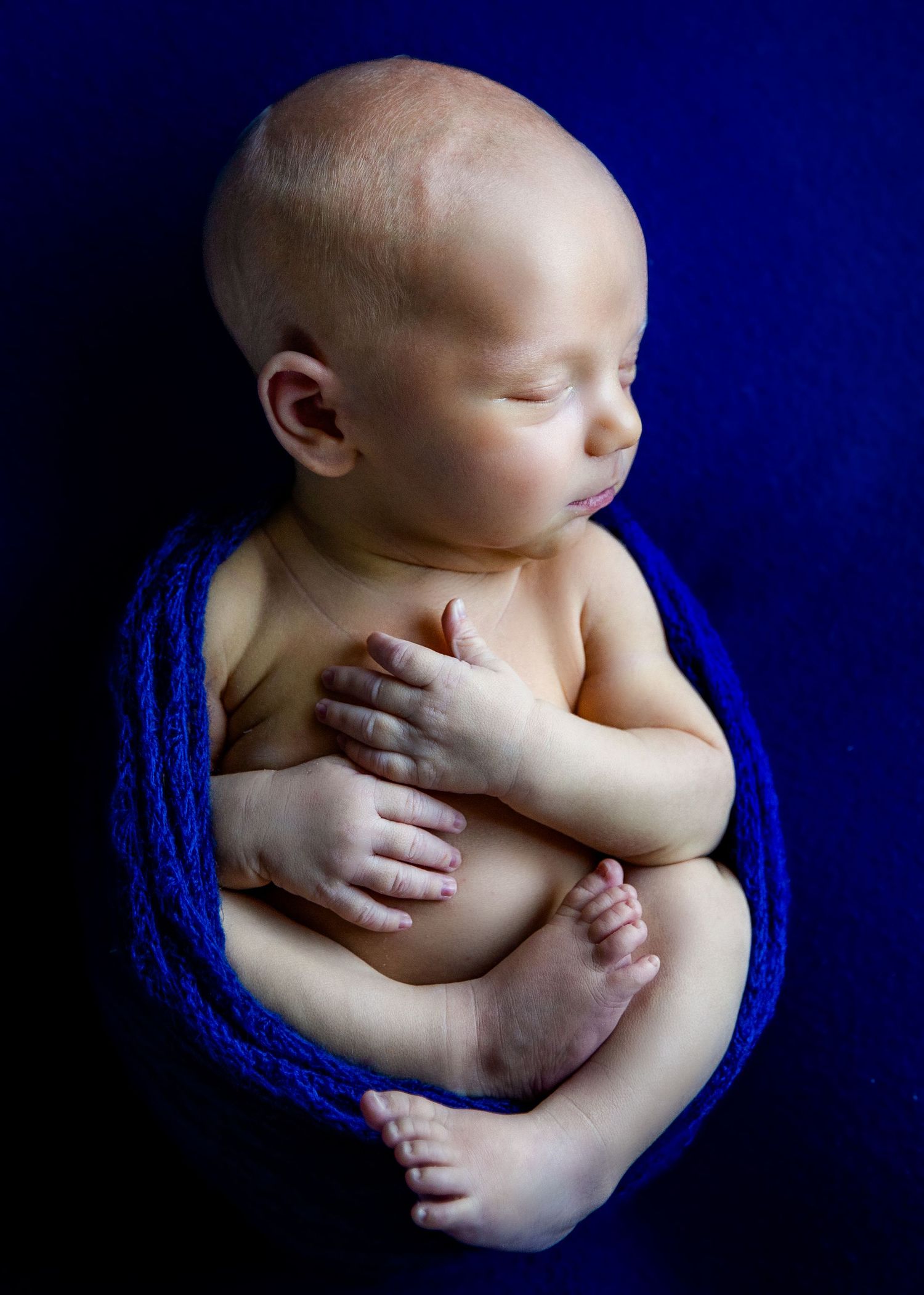 newborn baby boy in wrapped Huck Finn Pose with navy blue backdrop