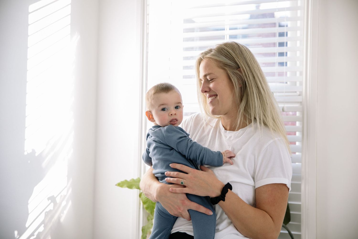 Parent and baby sharing joyful moment near bright window.